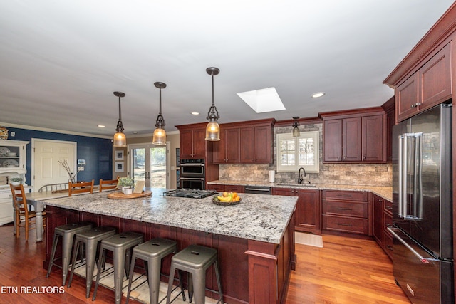 kitchen with a breakfast bar, appliances with stainless steel finishes, a skylight, a center island, and decorative light fixtures