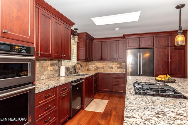 kitchen with sink, tasteful backsplash, appliances with stainless steel finishes, pendant lighting, and light stone countertops