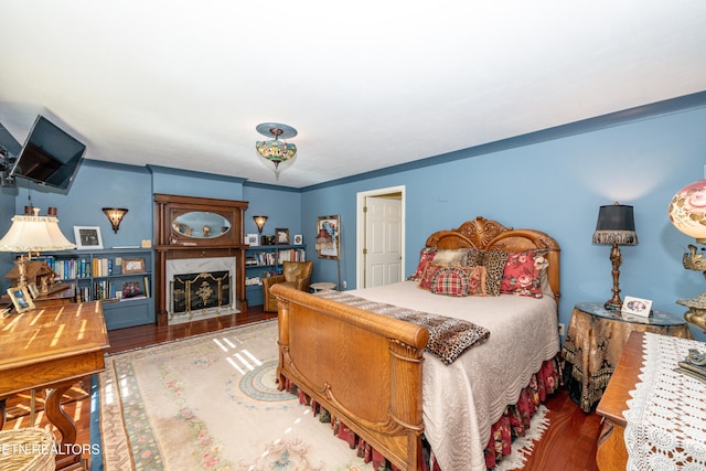 bedroom with ornamental molding, a premium fireplace, and dark hardwood / wood-style flooring