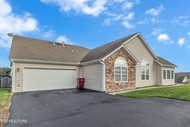 ranch-style home featuring central air condition unit, a front yard, a garage, stone siding, and driveway