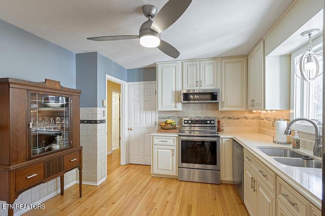 kitchen with sink, light wood-type flooring, appliances with stainless steel finishes, ceiling fan, and cream cabinetry