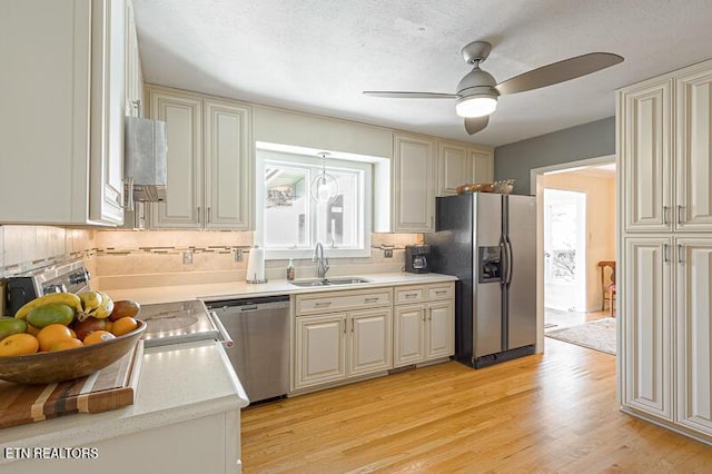 kitchen with sink, ceiling fan, stainless steel appliances, light hardwood / wood-style floors, and backsplash