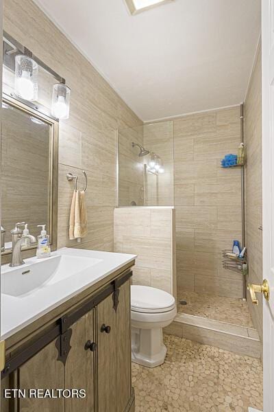 bathroom with vanity, tile walls, toilet, and tiled shower