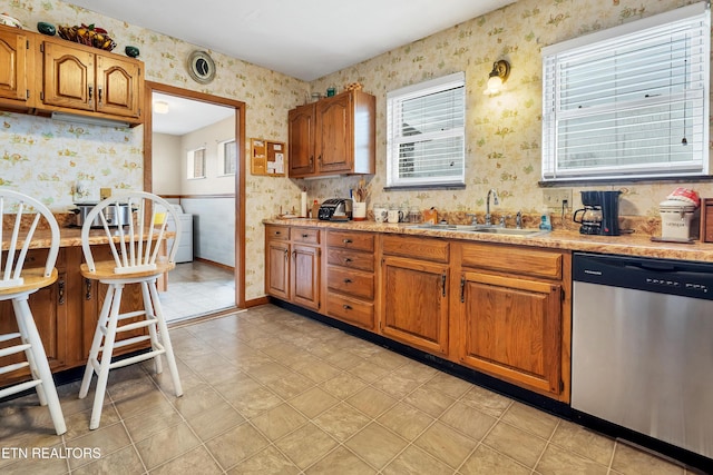 kitchen with a sink, light countertops, dishwasher, brown cabinetry, and wallpapered walls