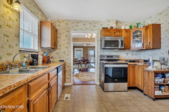 kitchen featuring brown cabinets, stainless steel appliances, light countertops, a sink, and wallpapered walls