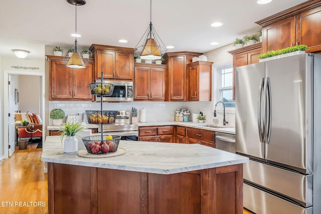 kitchen featuring sink, appliances with stainless steel finishes, hanging light fixtures, light stone counters, and decorative backsplash