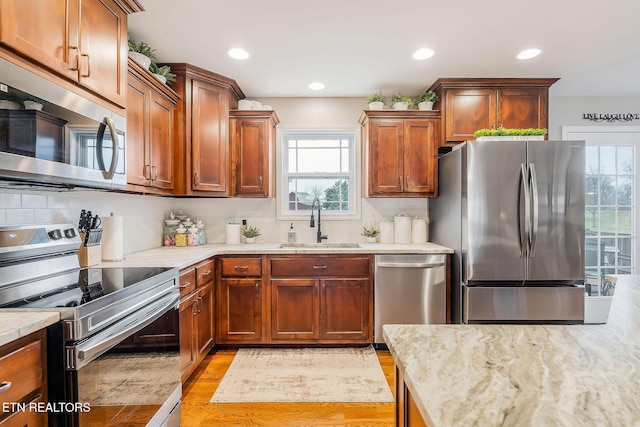 kitchen with sink, light wood-type flooring, stainless steel appliances, light stone countertops, and backsplash