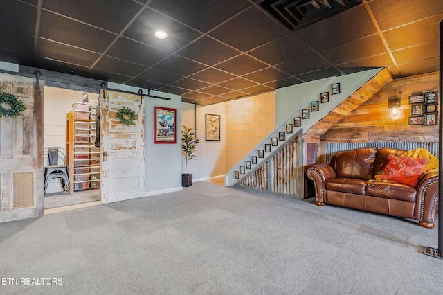 basement with a drop ceiling, a barn door, and carpet flooring