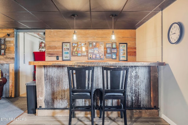 bar with a paneled ceiling, pendant lighting, and wood walls