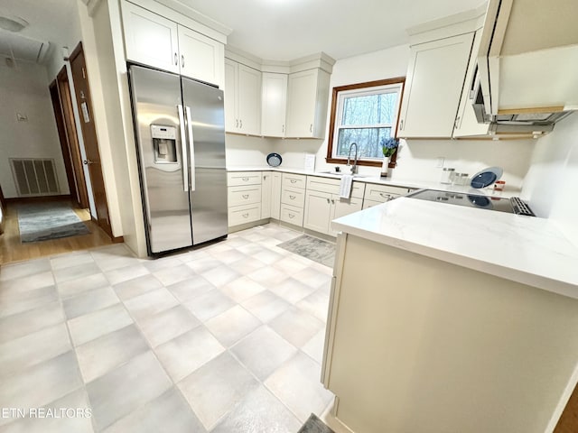 kitchen featuring light stone counters, stainless steel fridge, sink, and white cabinets