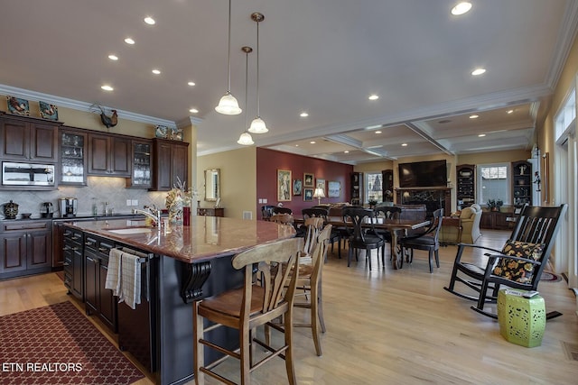 kitchen featuring dark brown cabinetry, a kitchen bar, stainless steel microwave, light stone countertops, and a kitchen island with sink