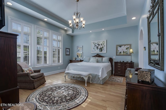 bedroom featuring crown molding, a raised ceiling, an inviting chandelier, and light wood-type flooring