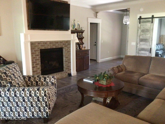 living room featuring ornamental molding, a barn door, dark hardwood / wood-style flooring, and a brick fireplace