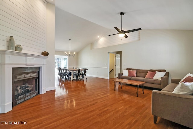 living room with high vaulted ceiling, ceiling fan with notable chandelier, wood finished floors, a fireplace, and baseboards