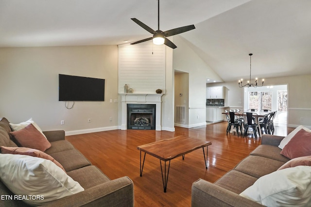 living area featuring ceiling fan with notable chandelier, wood finished floors, baseboards, and a fireplace