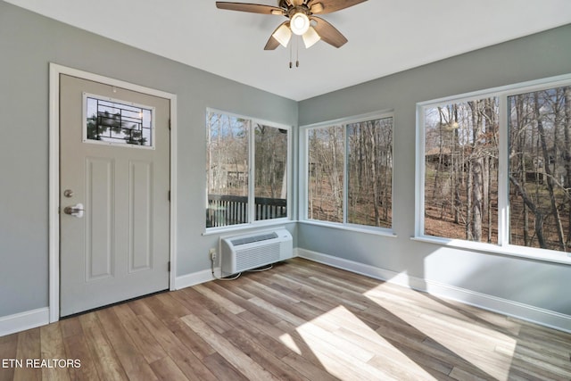 unfurnished sunroom featuring a wall unit AC and ceiling fan