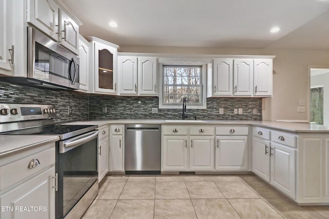 kitchen with a peninsula, stainless steel appliances, light tile patterned flooring, white cabinetry, and a sink