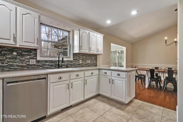 kitchen with a sink, light countertops, white cabinets, vaulted ceiling, and stainless steel dishwasher