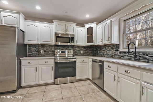 kitchen with a sink, tasteful backsplash, white cabinetry, stainless steel appliances, and light countertops