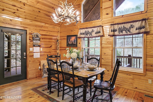 dining room featuring high vaulted ceiling, a chandelier, wooden walls, and light hardwood / wood-style flooring