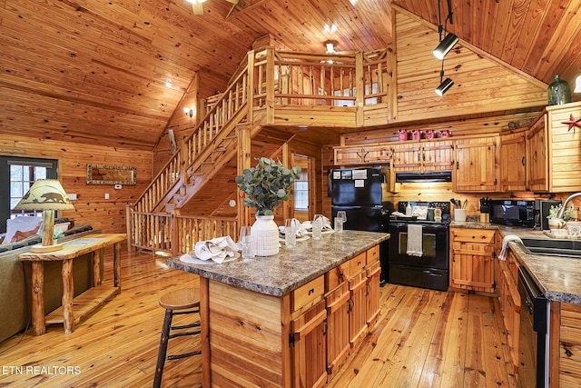 kitchen with extractor fan, a center island, wooden walls, light hardwood / wood-style floors, and black appliances