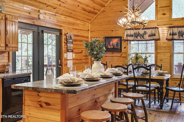 dining room with light hardwood / wood-style flooring, vaulted ceiling, wooden walls, and an inviting chandelier