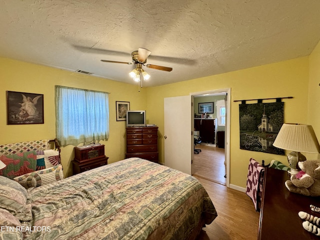 bedroom featuring ceiling fan, multiple windows, hardwood / wood-style floors, and a textured ceiling