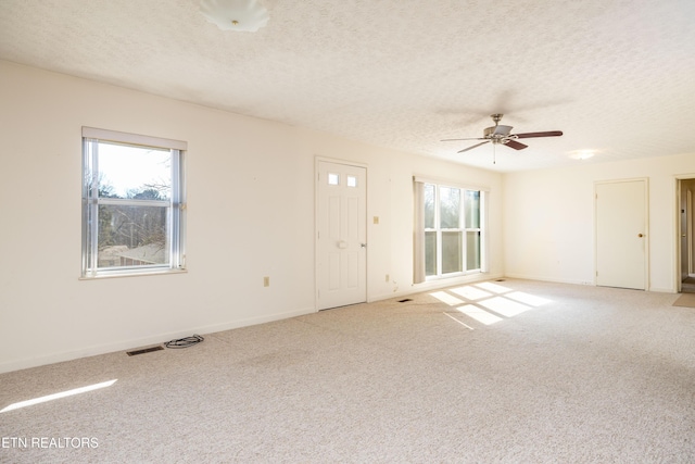 carpeted spare room with ceiling fan, a healthy amount of sunlight, and a textured ceiling