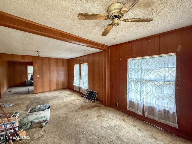 spare room with ceiling fan, light colored carpet, a textured ceiling, and wood walls