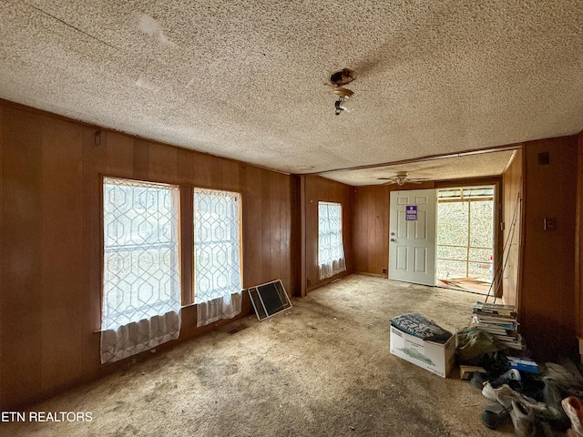 miscellaneous room featuring ceiling fan, wood walls, a textured ceiling, and carpet