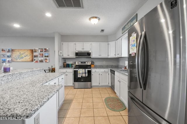 kitchen featuring white cabinetry, light stone counters, a textured ceiling, light tile patterned floors, and appliances with stainless steel finishes