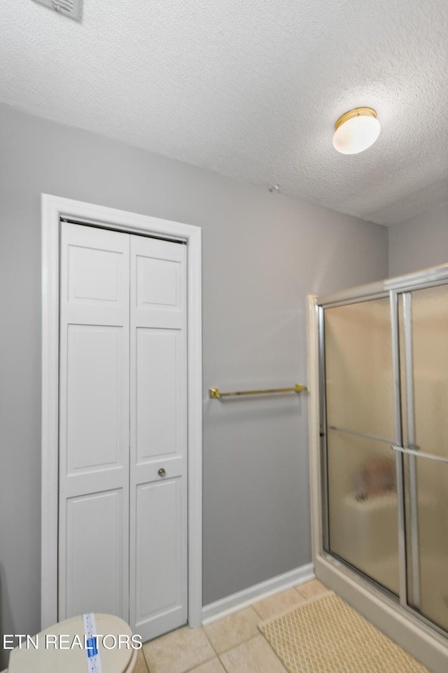 bathroom with tile patterned flooring, a textured ceiling, toilet, and walk in shower