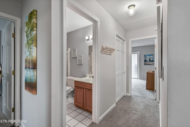 hallway featuring sink, light carpet, and a textured ceiling