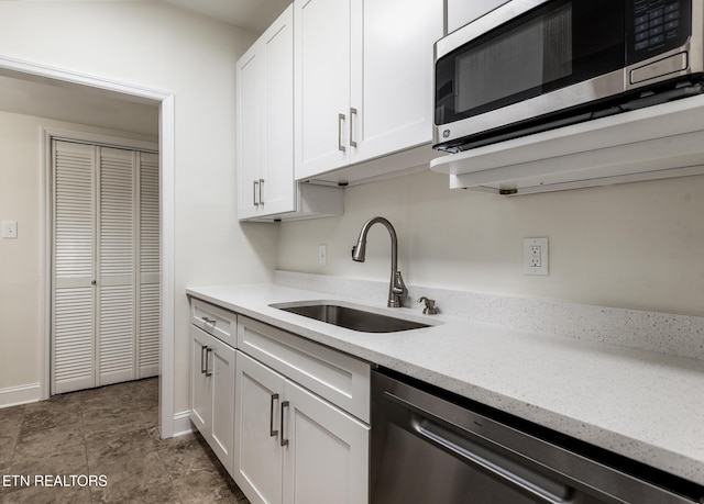 kitchen with light stone counters, sink, white cabinets, and black dishwasher