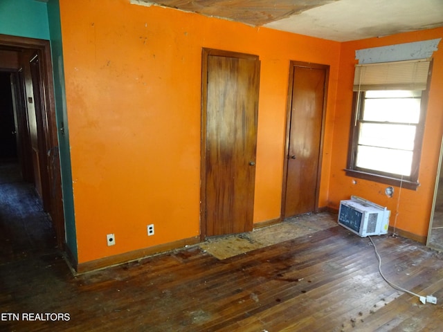 unfurnished bedroom with dark wood-style floors, a wall unit AC, baseboards, and multiple closets