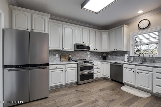 kitchen with sink, light hardwood / wood-style flooring, appliances with stainless steel finishes, white cabinets, and decorative backsplash