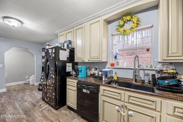 kitchen featuring black appliances, a sink, dark countertops, cream cabinets, and light wood-style floors