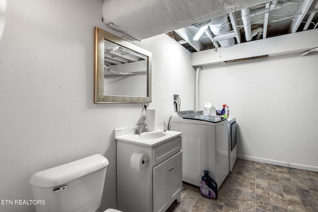 laundry area with washing machine and clothes dryer, stone finish flooring, baseboards, laundry area, and a sink