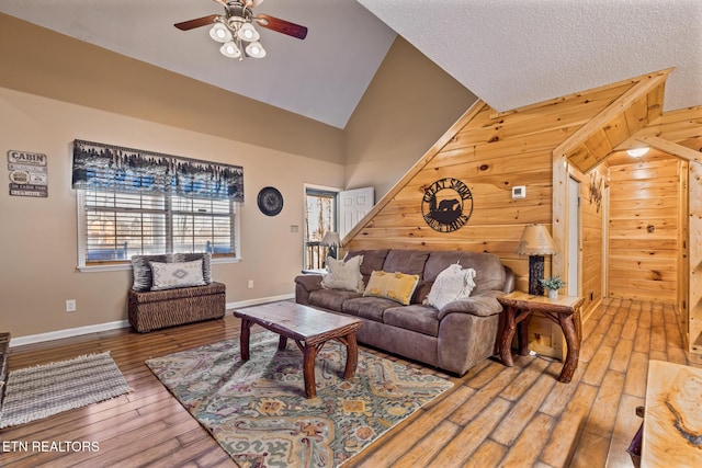 living room with wood-type flooring, ceiling fan, high vaulted ceiling, and wood walls