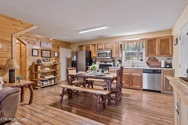 kitchen featuring sink, stainless steel appliances, wood walls, and light wood-type flooring