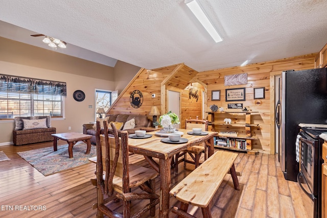 dining room featuring wooden walls, a textured ceiling, and light wood-type flooring