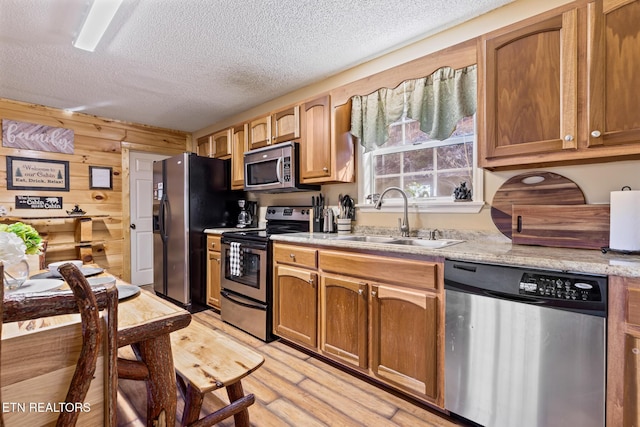 kitchen with sink, appliances with stainless steel finishes, wooden walls, a textured ceiling, and light wood-type flooring