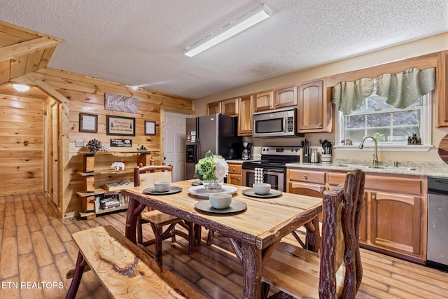 kitchen featuring appliances with stainless steel finishes, light wood-type flooring, wooden walls, and light stone counters