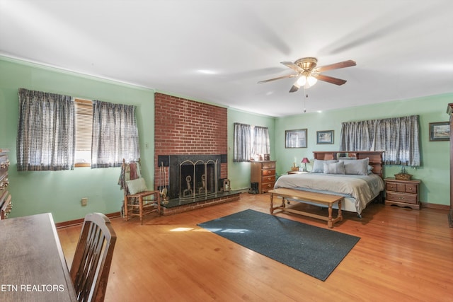 bedroom featuring wood-type flooring, a brick fireplace, ornamental molding, and ceiling fan