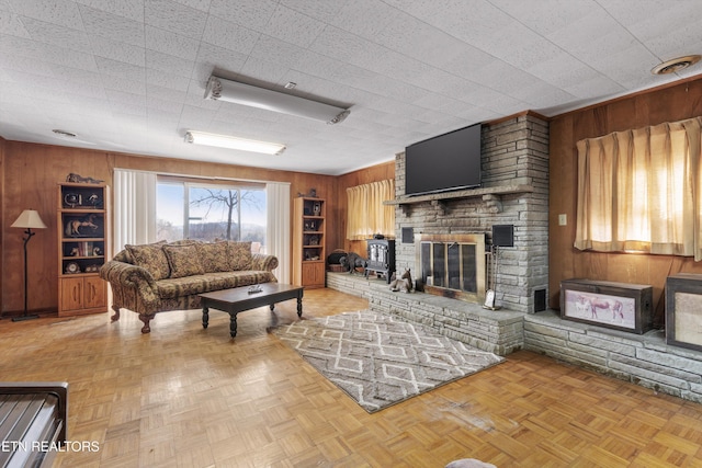 living room with light parquet floors, a large fireplace, and wood walls