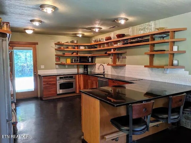 kitchen with appliances with stainless steel finishes, sink, a kitchen breakfast bar, decorative backsplash, and kitchen peninsula