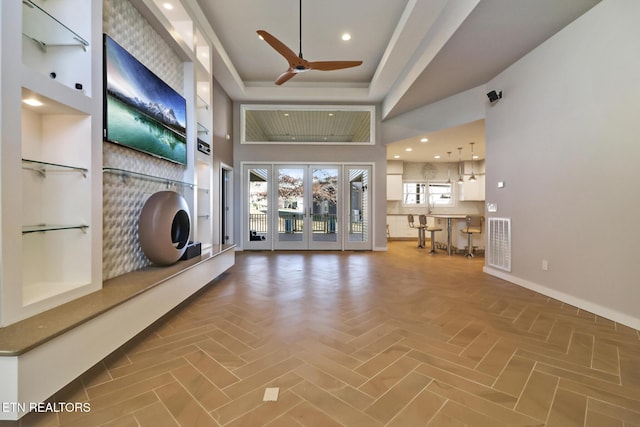 unfurnished living room featuring french doors, parquet flooring, ceiling fan, a tray ceiling, and a towering ceiling