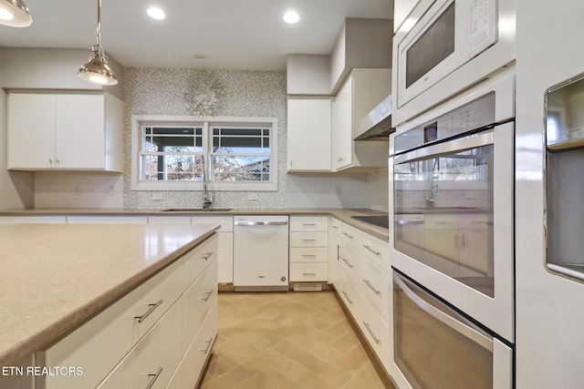 kitchen featuring sink, white appliances, white cabinetry, hanging light fixtures, and backsplash