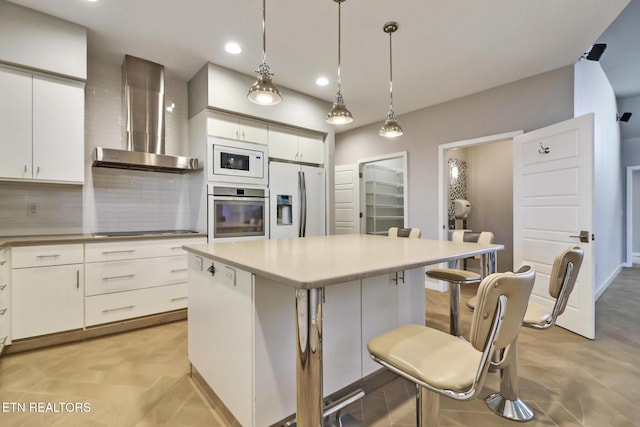 kitchen featuring appliances with stainless steel finishes, pendant lighting, white cabinets, a center island, and wall chimney exhaust hood