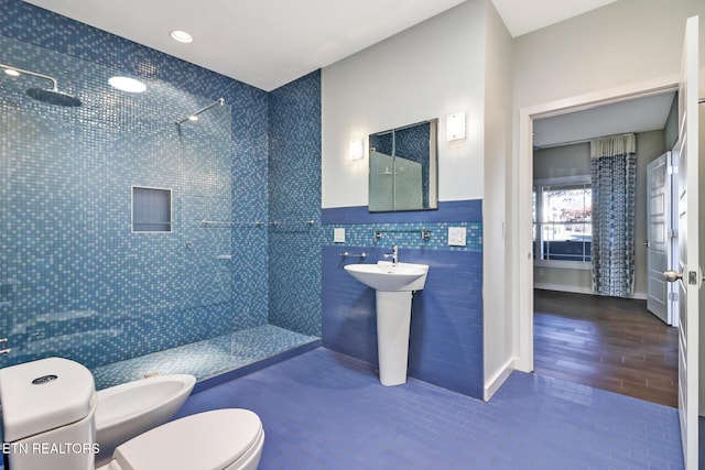 bathroom with a bidet, sink, tile walls, a tile shower, and toilet